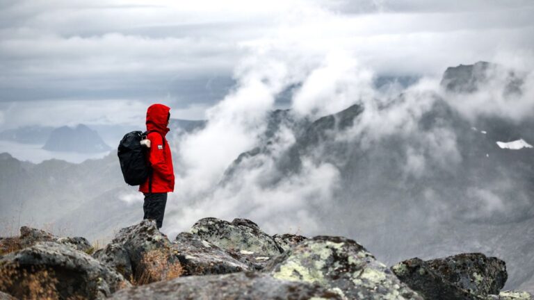 Escursionista con giacca da trekking rossa impermeabile tra le nuvole in montagna
