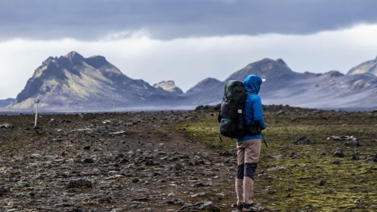 Escursionista con zaino da trekking cammina su un sentiero roccioso in un paesaggio vasto